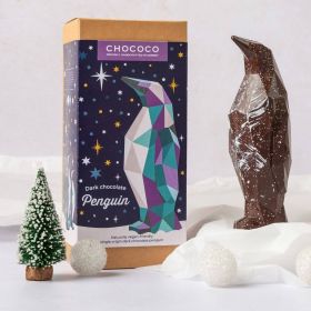 Dark chocolate geometric penguin by Chococo looking up to a north star silver Christmas decoration in a snowy forest with Christmas trees around 