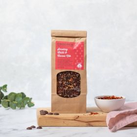 Dark Chocolate Oaky-smokey Chilli & Nib Slabs which are  vegan-friendly by Chococo on a wooden chopping board with chilli flakes in a white pot and pink linen napkin 