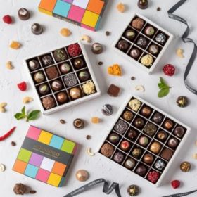 A stacked cascade of Chococo chocolate boxes with fresh milk chocolates around.  