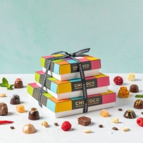 A stacked cascade of Chococo chocolate boxes with fresh milk chocolates around.  