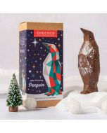 Milk chocolate geometric penguin by Chococo looking up to a north star silver Christmas decoration in a snowy forest with Christmas trees around 