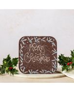 giant dark chocolate bar with hand pipped Merry Christmas message. hand decorated with holly design and surrounded by holly, on a marble plate and linen napkin 